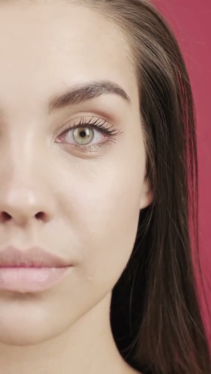 A close-up of half a face against a saturated pink background, one green eye and part of the mouth in frame