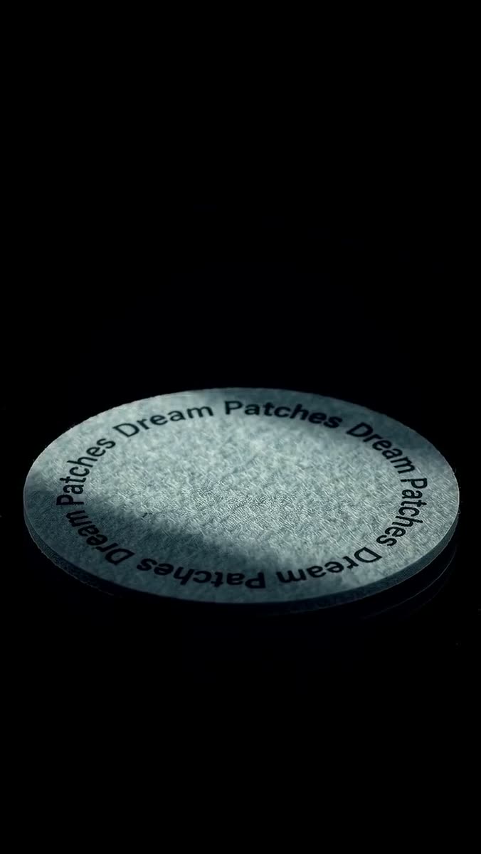 A gray Ephoria dream patch disc lying on a black reflective surface, its edge catching a soft highlight
