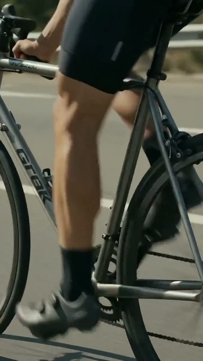 A cyclist's legs mid-pedal on a road bike, shot from the side against sunlit tarmac