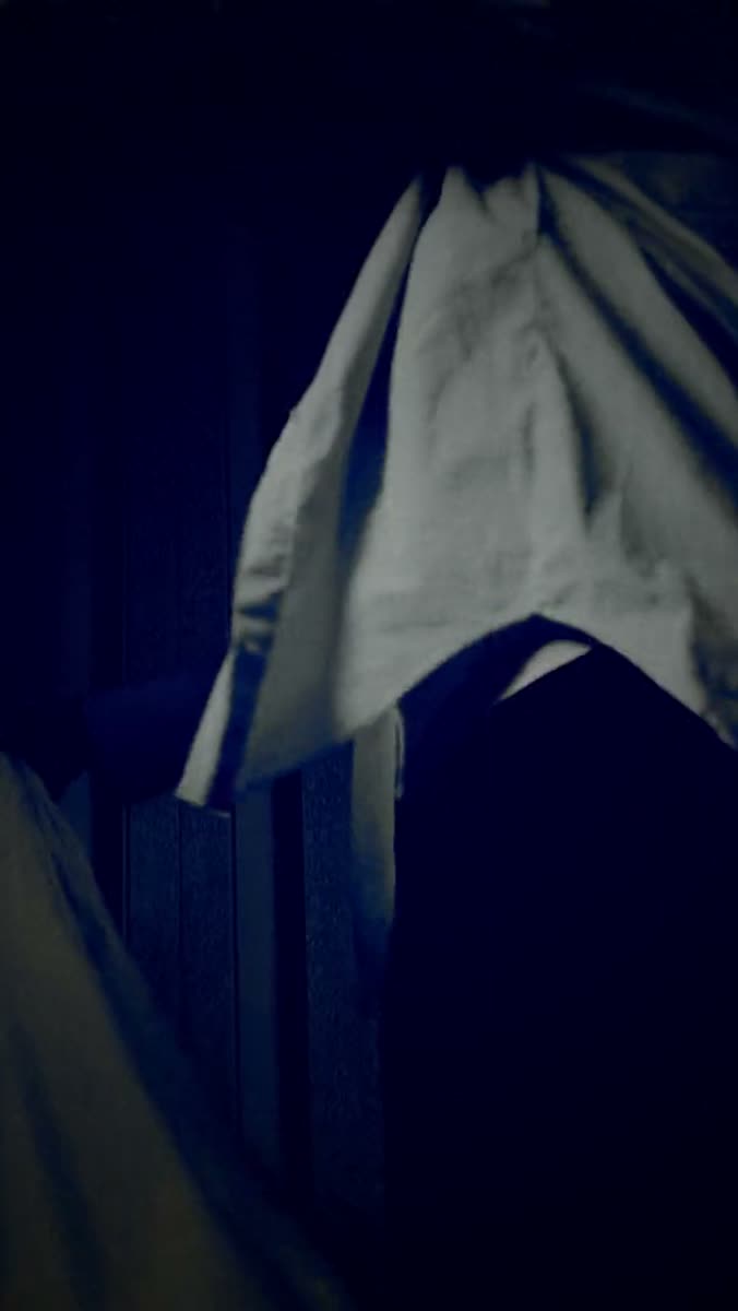 A white shirt hanging in near darkness against a deep blue wall, its folds catching the only light in the frame