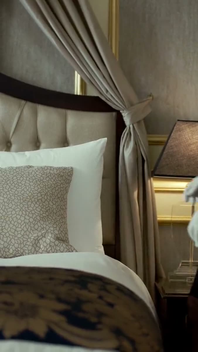 A hotel suite: a canopy bed with a buttoned cream headboard, a folded quilt across the foot, and a lamp lit on the nightstand